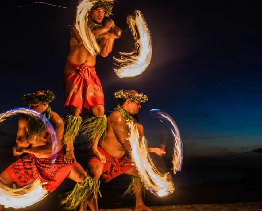 Three performers in traditional attire dance with fire at night.