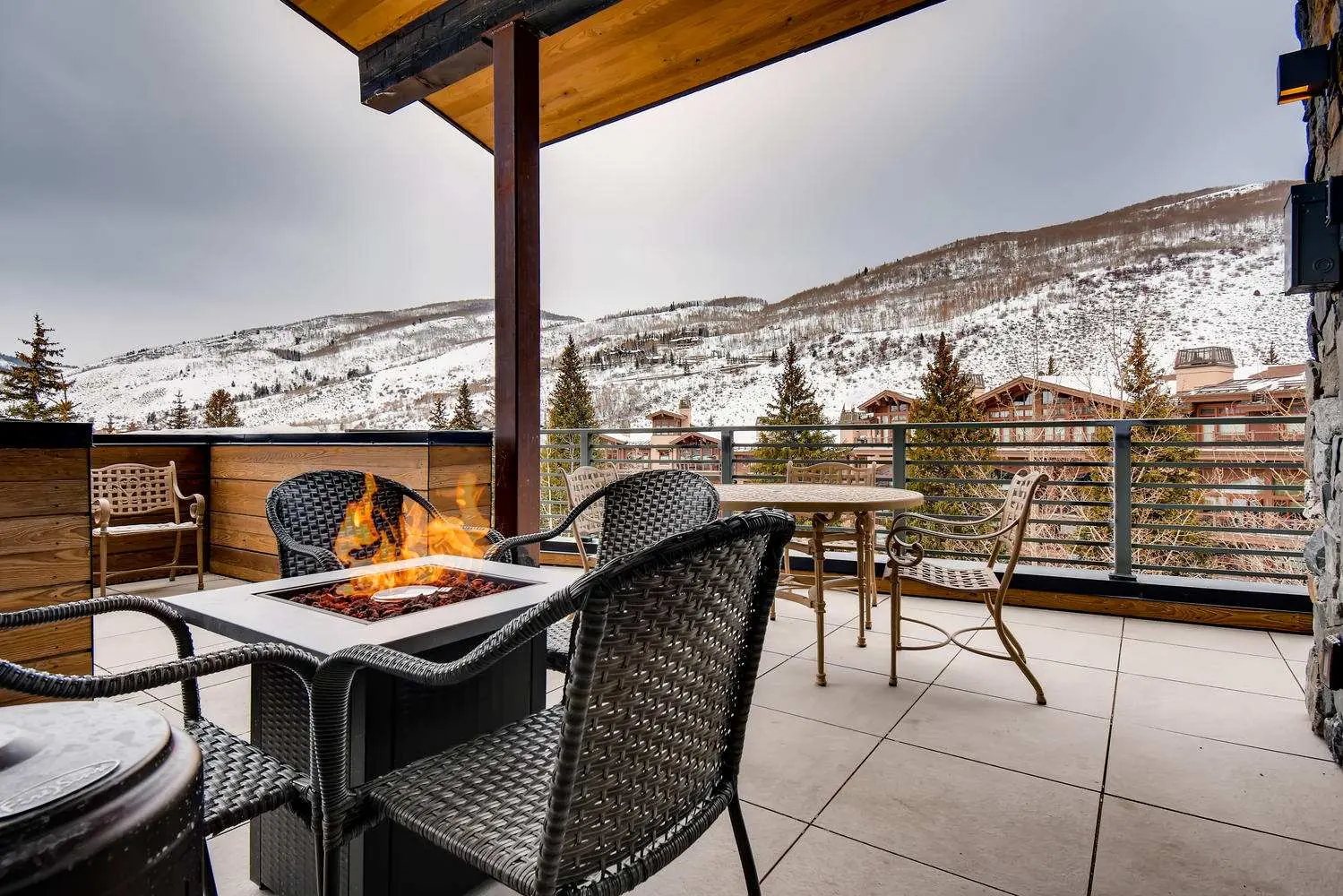 Outdoor patio with wicker chairs and a fire table overlooking a snowy mountain landscape.