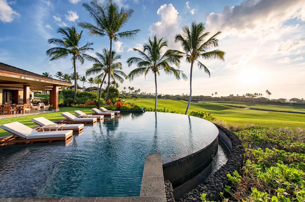A luxury villa with an infinity pool overlooking a golf course and palm trees at sunset.