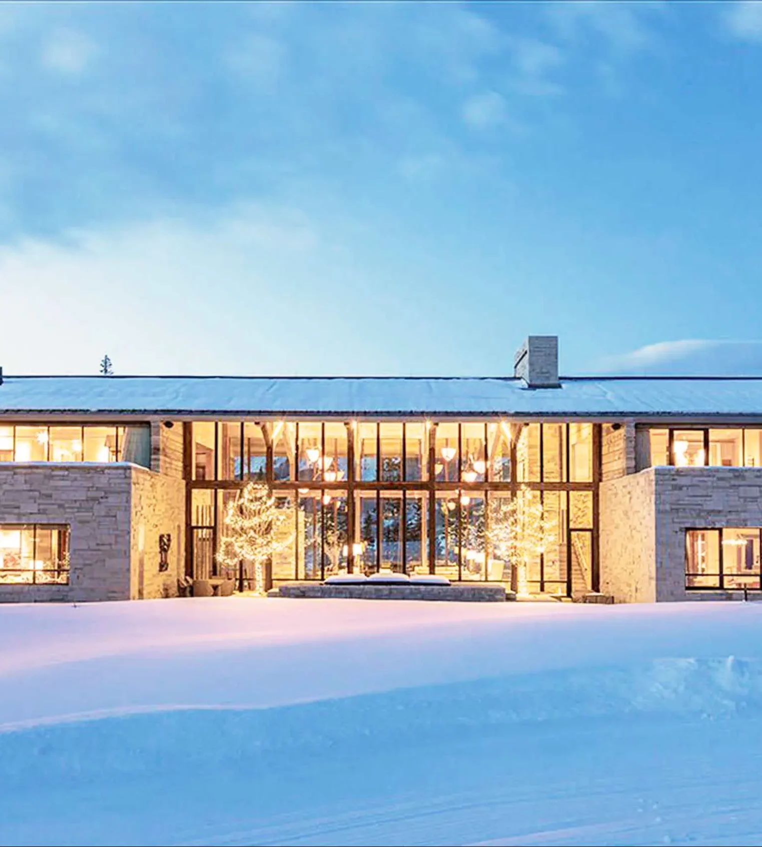 Luxury villa with large windows, surrounded by snow, illuminated at night.