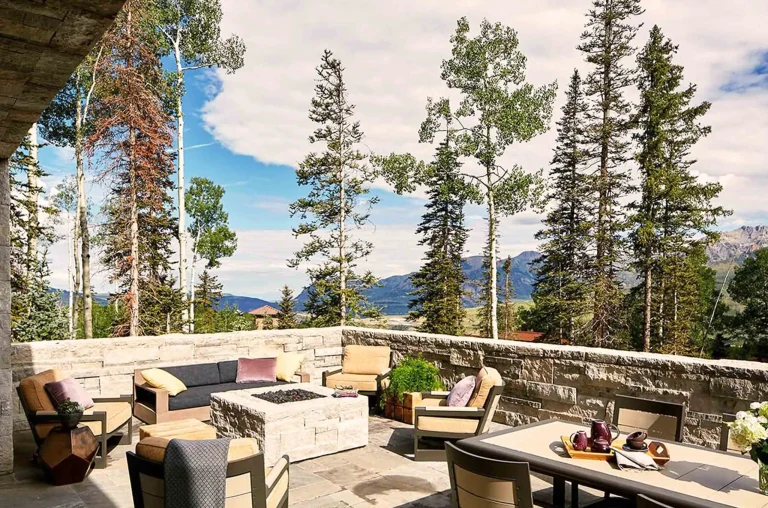 Outdoor patio with seating area and fire pit, surrounded by tall trees and mountain views.