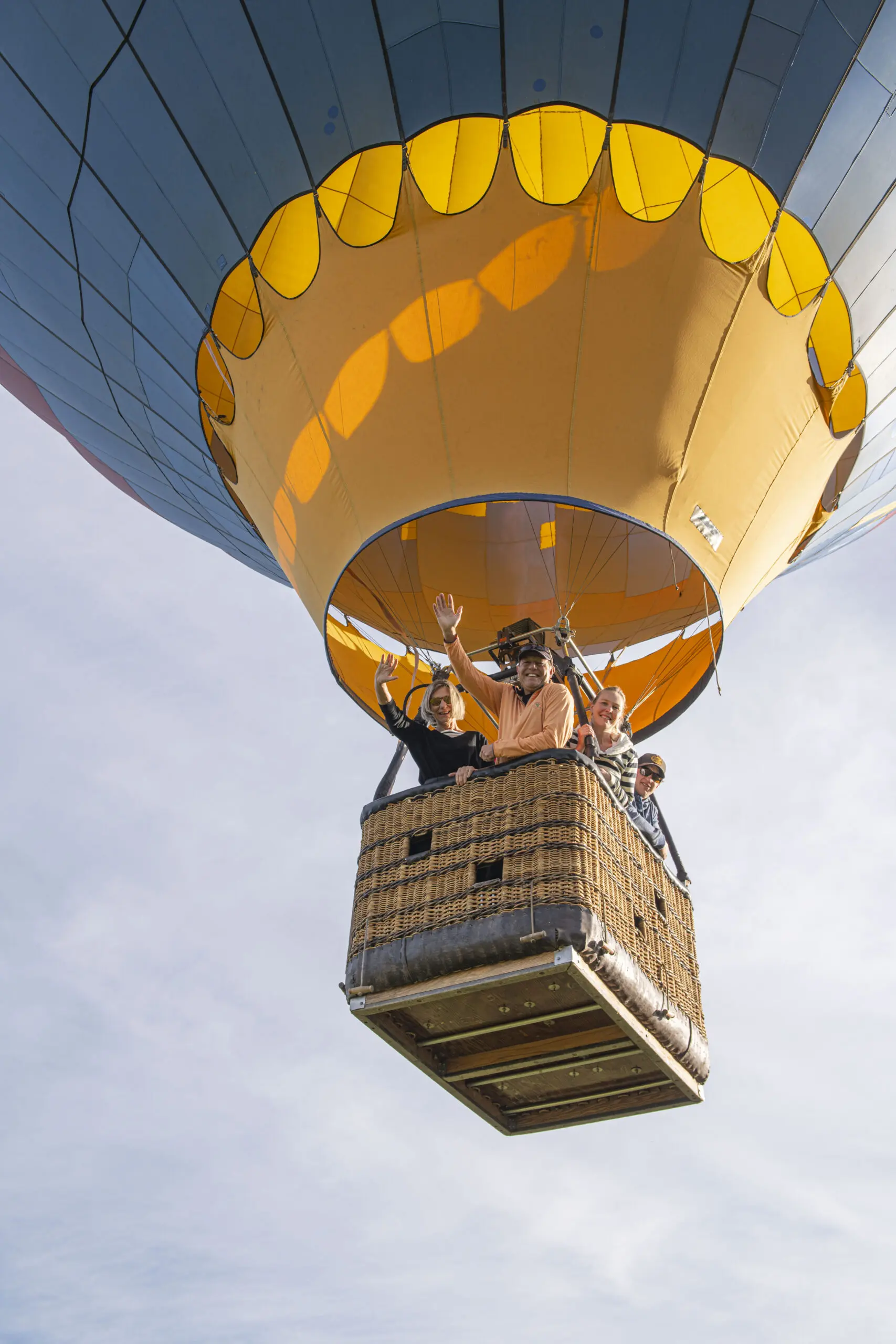 People waving from a hot air balloon basket with a colorful canopy in the sky.