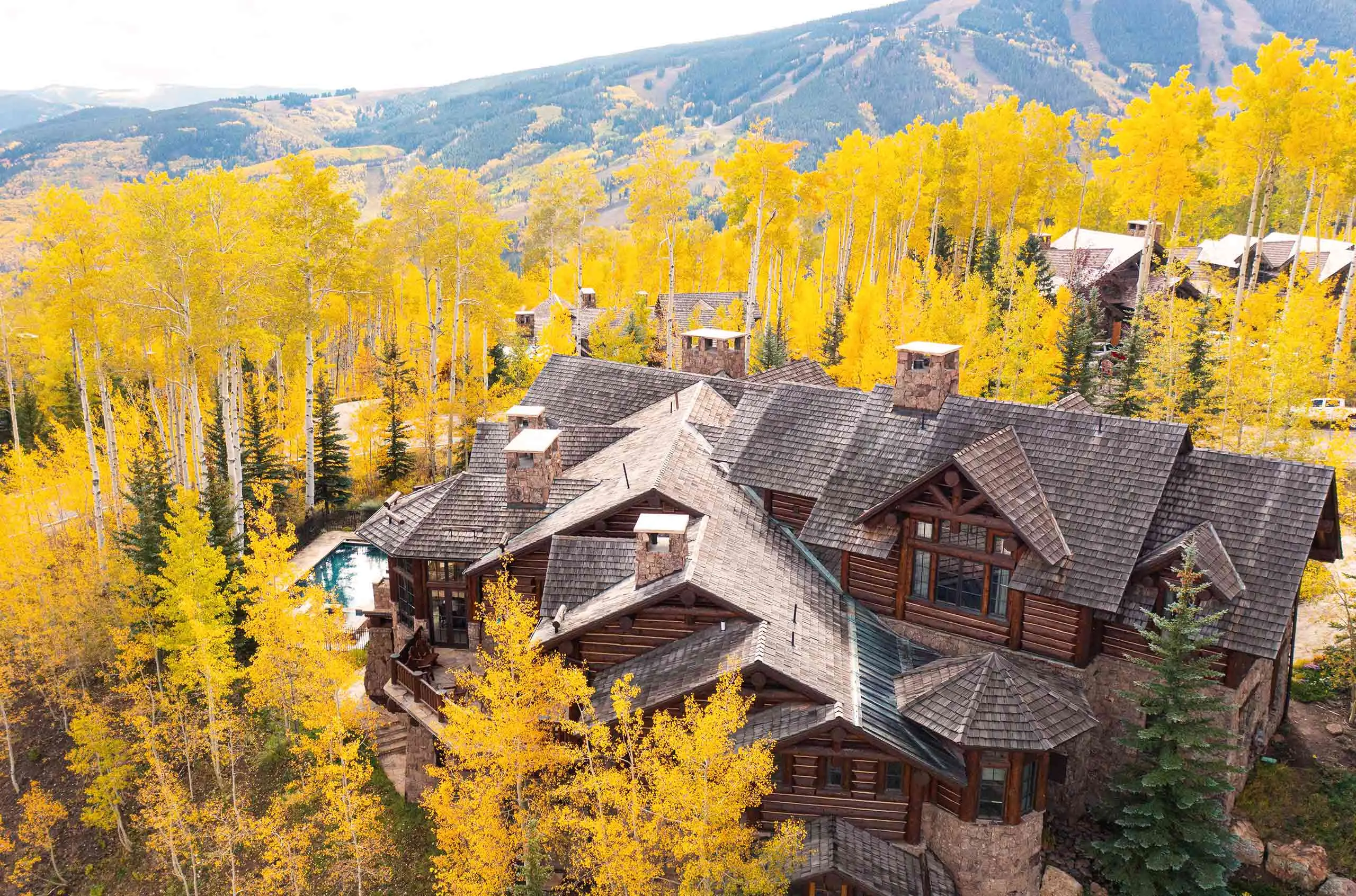 Luxurious villa nestled among vibrant autumn trees with mountain views in the background.
