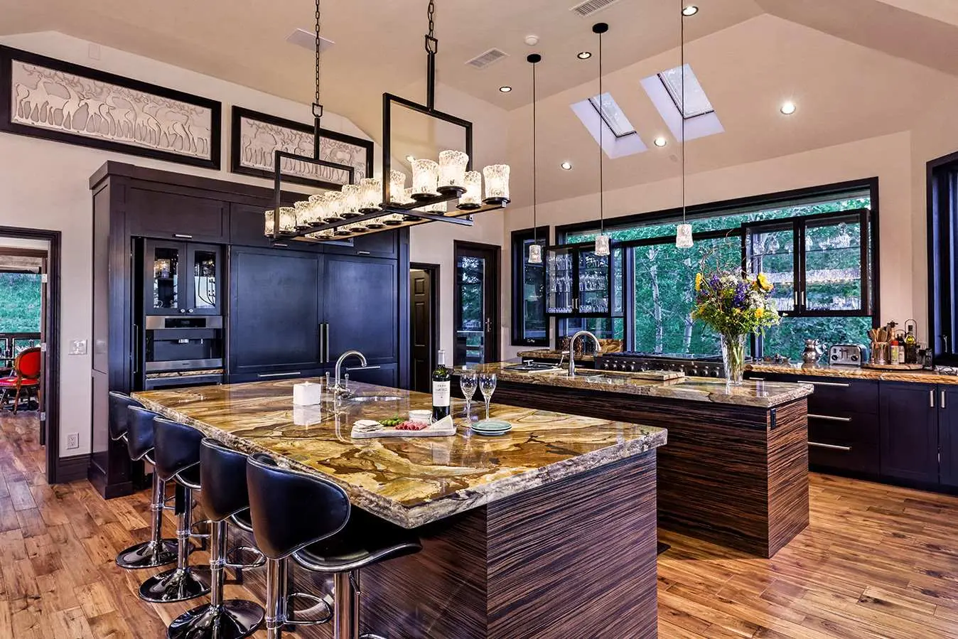 Luxurious kitchen with large marble islands, modern black cabinetry, pendant lighting, and skylights.