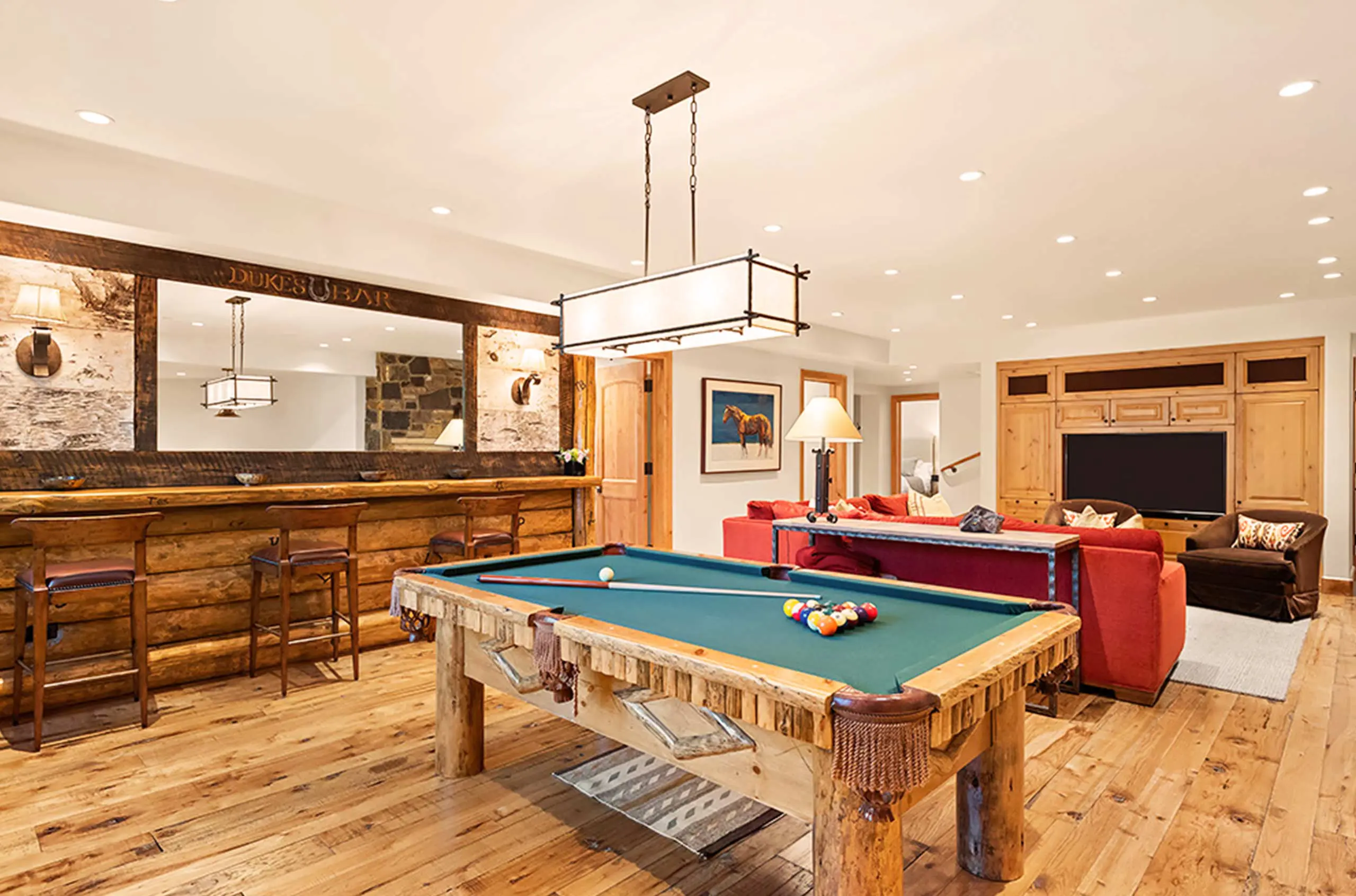 Recreational room with a rustic pool table and bar area featuring wooden stools, large mirror, and cozy seating.