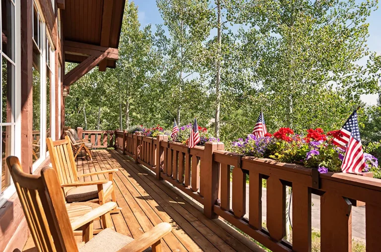 Wooden deck with chairs and flower boxes, decorated with American flags, surrounded by trees.