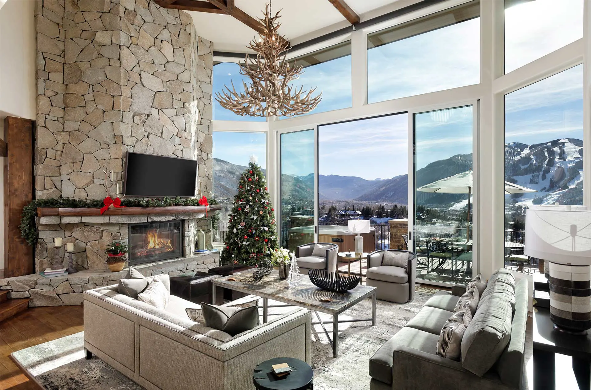 Luxurious living room with stone fireplace, Christmas decorations, modern furniture, and large windows with a mountain view.