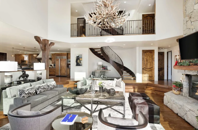 Luxury villa interior with elegant furnishings, a grand chandelier, spiral staircase, and stone fireplace.