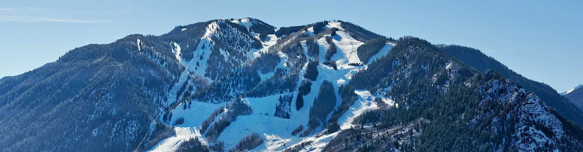 Snow-covered mountainous landscape with ski slopes and forested areas.