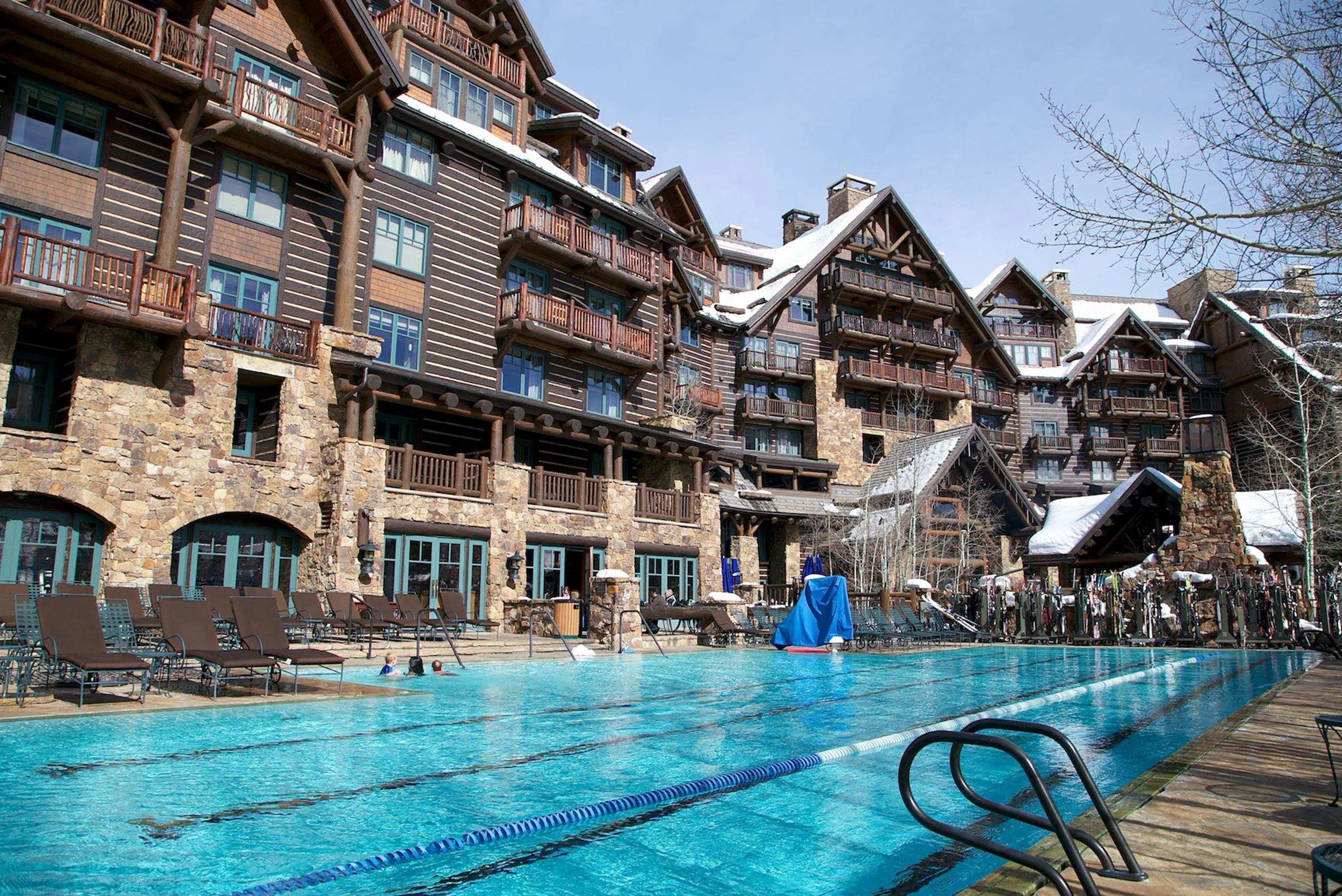 Luxurious wooden lodge with a large outdoor swimming pool, surrounded by snow-covered landscape.