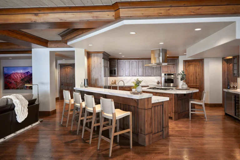 Luxury kitchen with wooden cabinets, a large marble island, bar stools, and hardwood flooring.