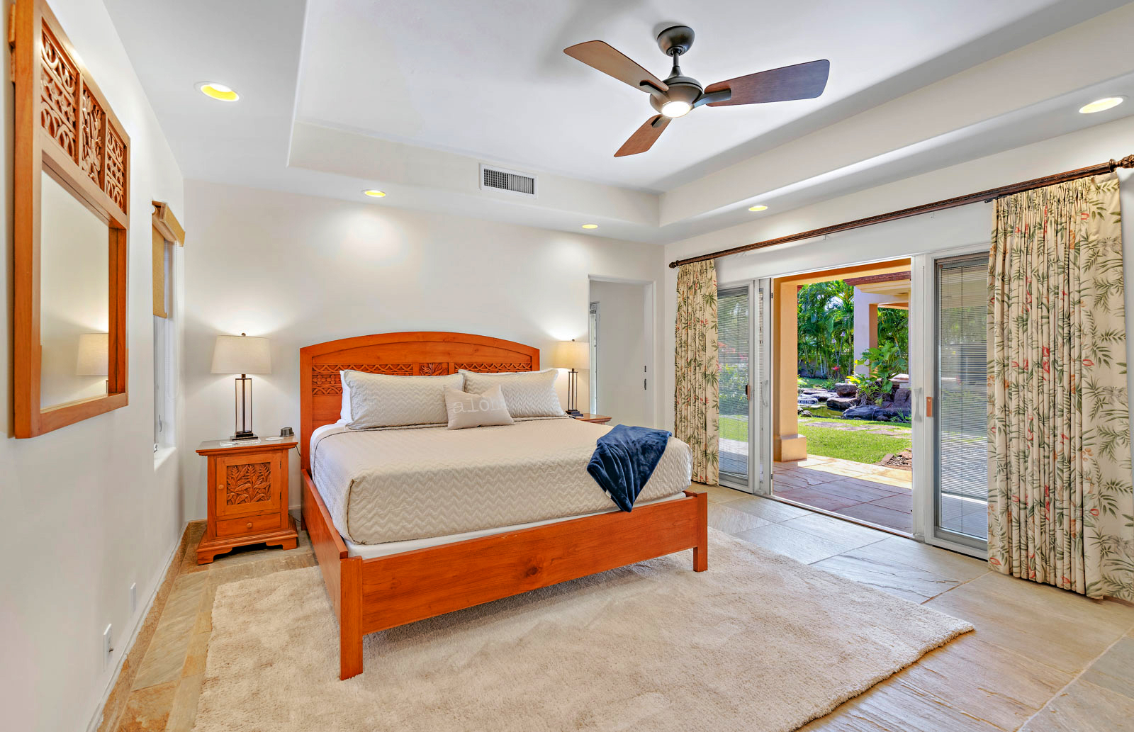 Bedroom with wooden bed, ceiling fan, and sliding doors opening to a garden.