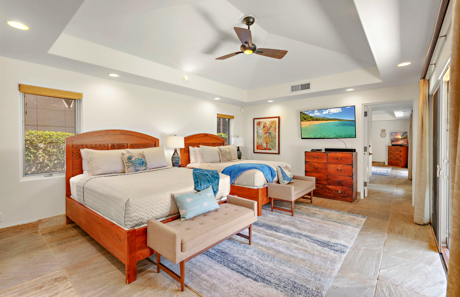 Spacious bedroom with two wooden beds, modern decor, a ceiling fan, art on the wall, and a flat-screen TV.