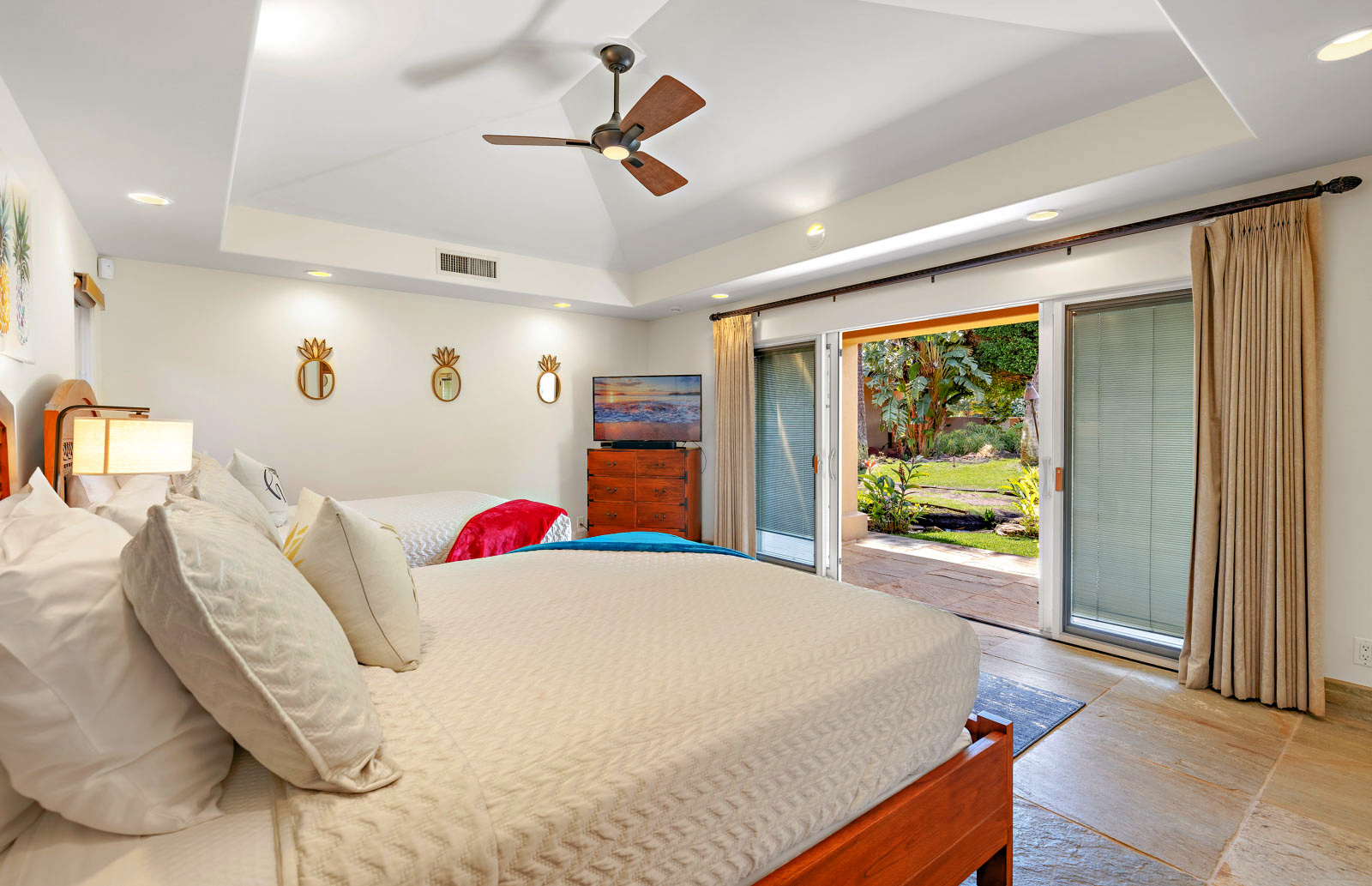 Bedroom with two beds, ceiling fan, wall-mounted TV, and open sliding doors leading to a garden.