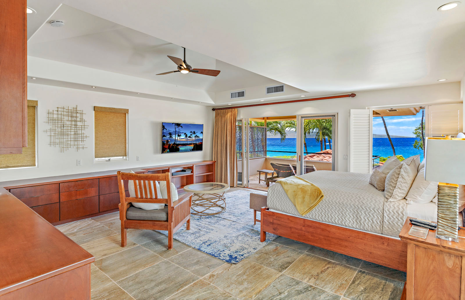 Spacious bedroom with wooden furniture, tiled floor, and an open view of the ocean through large patio doors.
