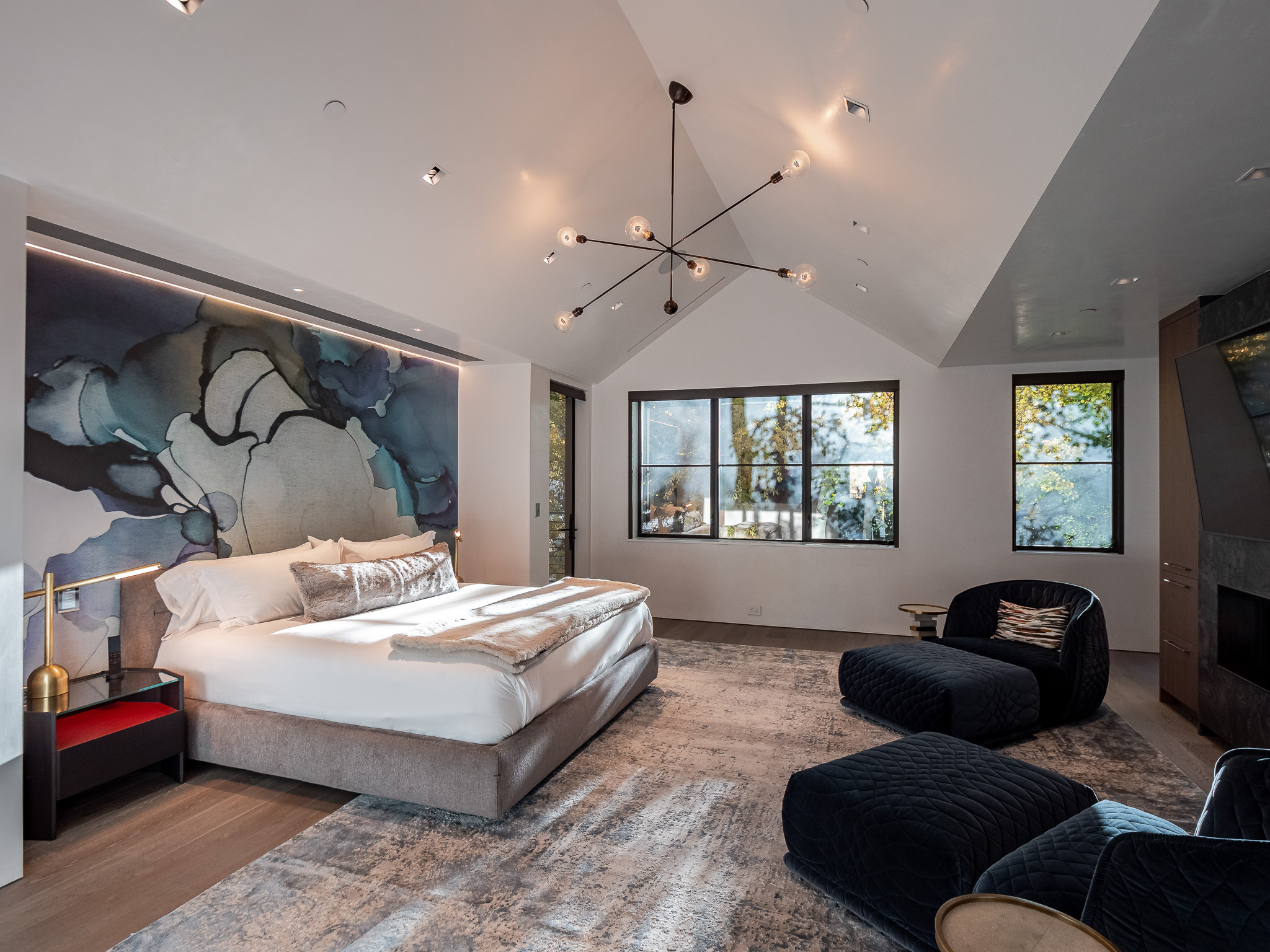 Luxurious bedroom with a large bed, abstract wall art, vaulted ceiling, modern chandelier, and comfortable seating in a villa rental in Aspen, Colorado.
