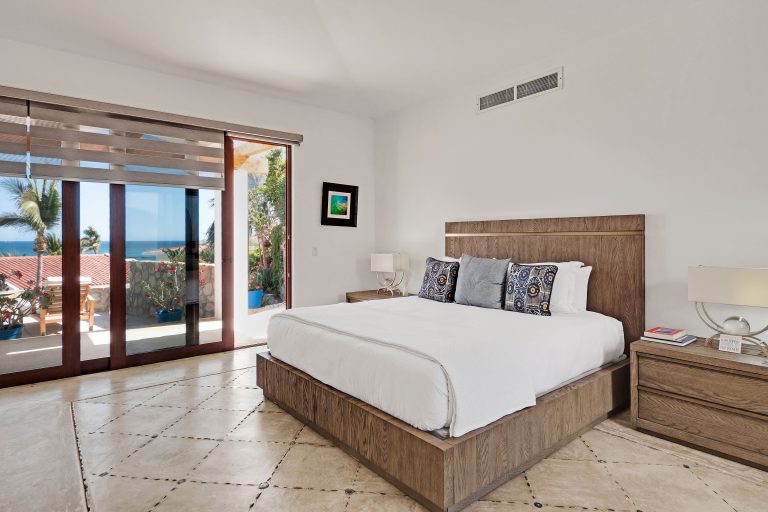 Luxury villa bedroom with ocean view and modern decor, featuring a large bed, wooden furniture, and glass doors opening to a terrace.