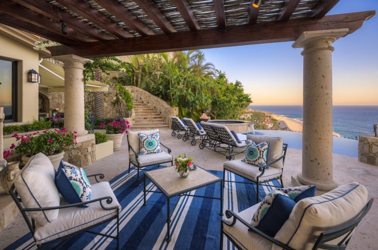 Spacious outdoor patio of a luxury villa in Los Cabos with comfortable seating, decorative pillows, potted plants, and ocean view.