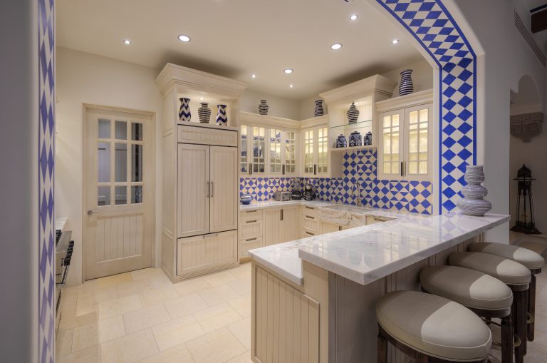 Luxurious kitchen with blue and white tile accents, marble countertops, beige cabinetry, and modern appliances.
