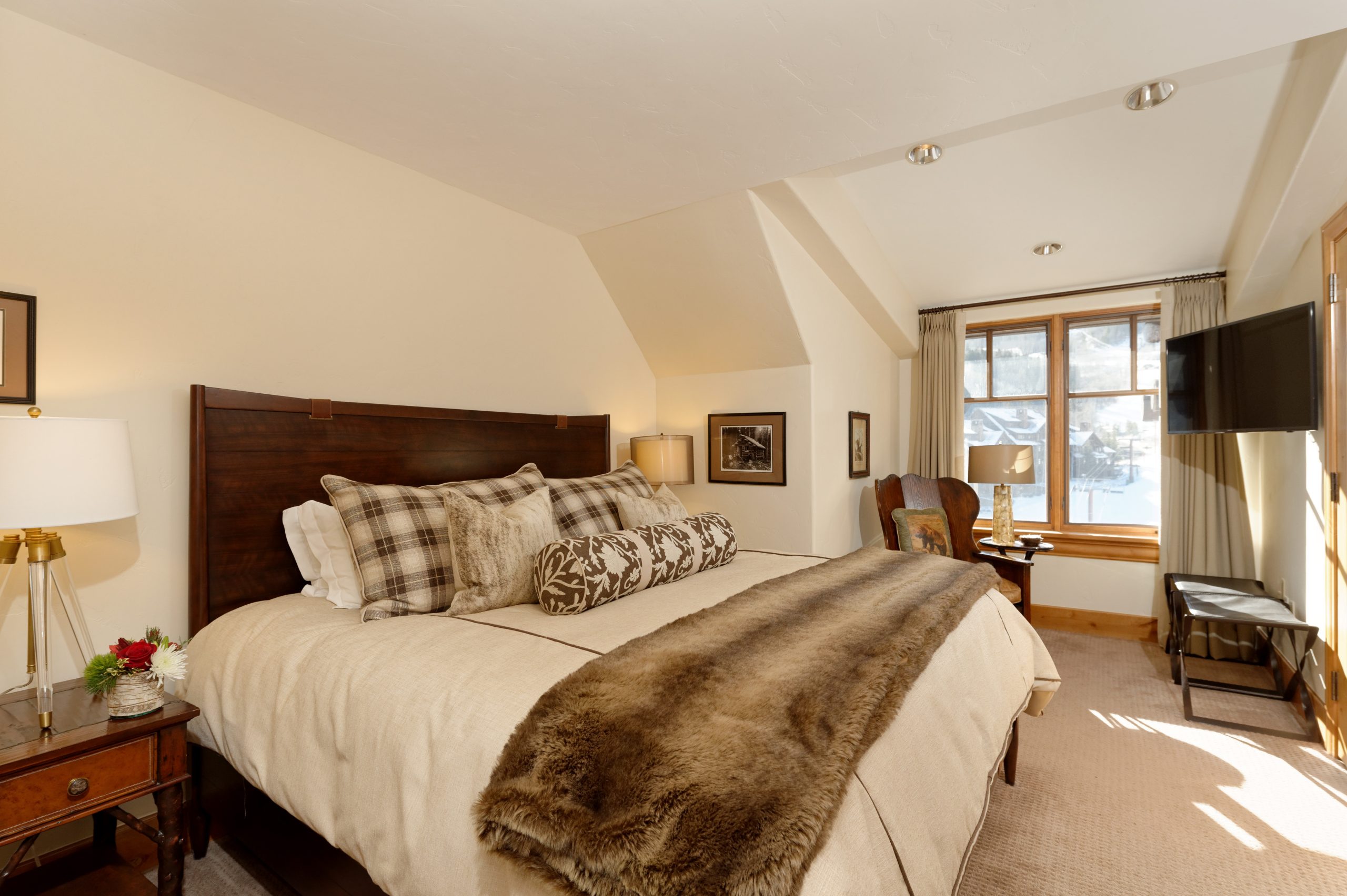 Luxurious bedroom interior with a plush bed, fur throw, and window view of snowy mountains.