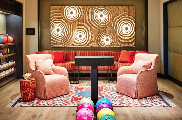 Colorful and cozy living area with patterned rug, armchairs, vibrant pillows, and artistic wall decoration, featuring bowling balls on a wooden floor.