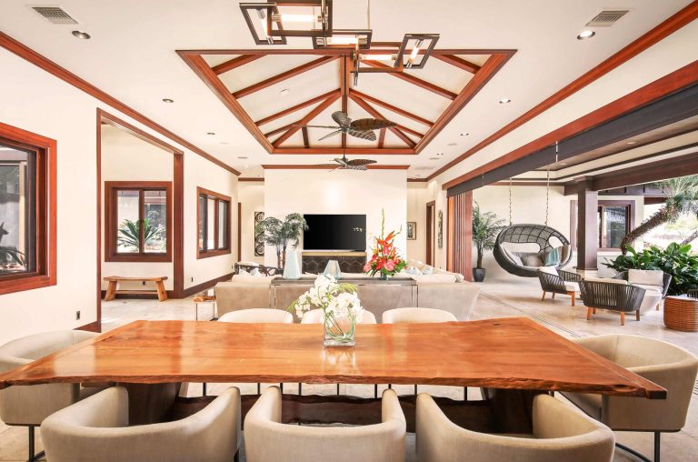 Luxuriously furnished villa interior with a large wooden dining table, modern seating, and open-air lounge area, featuring tropical plants and elegant decor.