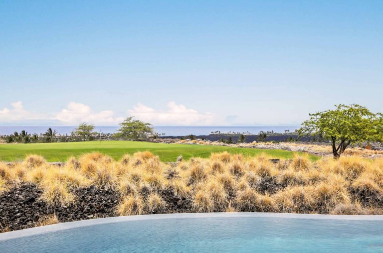 Infinity pool overlooking a golf course and ocean in Hawaii with clear blue skies.
