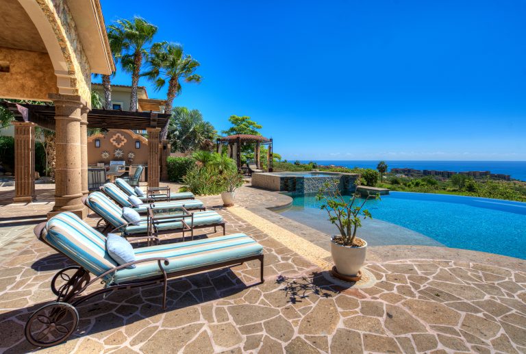 Luxury villa with patio, lounge chairs, infinity pool, and ocean view in Los Cabos, Mexico.