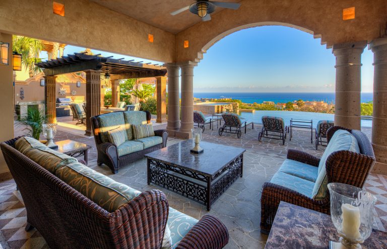 Spacious outdoor patio of a luxury villa with ocean views in Los Cabos, featuring comfortable seating, a dining area under a pergola, and an infinity pool.