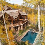 A luxurious log cabin villa surrounded by autumn aspen trees, with a stone patio and a swimming pool, located in Beaver Creek, Colorado.