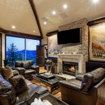 Luxurious living room with leather sofas, a fireplace, large paintings, and mountain views through large windows in Aspen, Colorado.