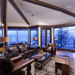 Luxurious living room with leather furniture, a stone fireplace, wood floors, large windows, and scenic mountain views.