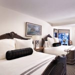 Luxurious bedroom with two ornate beds, a painting on the wall, and large windows showcasing a snowy mountain view.