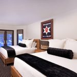 A luxurious bedroom with two double beds, wooden furniture, and large windows displaying a snowy mountain view.