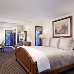 A luxurious bedroom with a large wooden bed, elegant furniture, lamps, and windows overlooking a snowy mountain view.