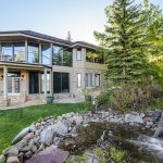 Luxury villa with large windows, surrounded by trees and a landscaped garden with a rock waterfall in Aspen, Colorado.