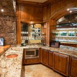 Luxurious villa kitchen with stone and wood finishes, a granite countertop, mirrored shelving with glassware, and a microwave.