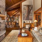 Rustic living room with stone fireplace, wooden beams, plush seating, and a large painting on the wall.