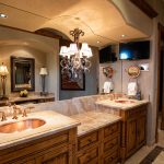 Luxurious bathroom with wooden cabinets, dual copper sinks, a large mirror, chandelier lighting, and decorative lamps.