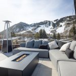 Outdoor seating area with a modern gas fire pit, overlooking snowy mountains and ski slopes in Aspen, Colorado.