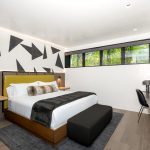 Modern bedroom with geometric wall art, a plush bed, desk area, and large windows in a luxury villa.
