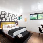 Modern bedroom with a king-sized bed, abstract wall art, and a window view of greenery in a luxury villa rental in Aspen, Colorado.