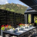 Outdoor dining area with a set table, surrounded by black lattice fences, colorful flowers, and mountain views in Aspen, Colorado.