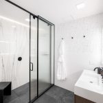Modern bathroom with a glass-enclosed shower, white marble walls, black accents, and a sleek sink with a backlit mirror.