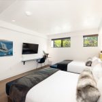 Bright, modern bedroom with two beds, wall art, TV, desk, and large windows.