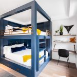 Bunk beds with navy blue frames and gold railings in a modern bedroom, featuring a built-in desk and shelves with decor and books.