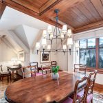 Dining room with a wooden table, chairs, and a chandelier, featuring large windows with a snowy mountain view.