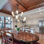 Dining area with wooden table and chairs, chandelier, and a view of a modern kitchen in a luxury villa.