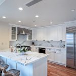 Modern kitchen with marble countertops, stainless steel appliances, and wooden bar stools.
