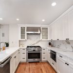 Luxury kitchen with white cabinetry, marble countertops, and stainless steel appliances, featuring a scenic forest view through the window.